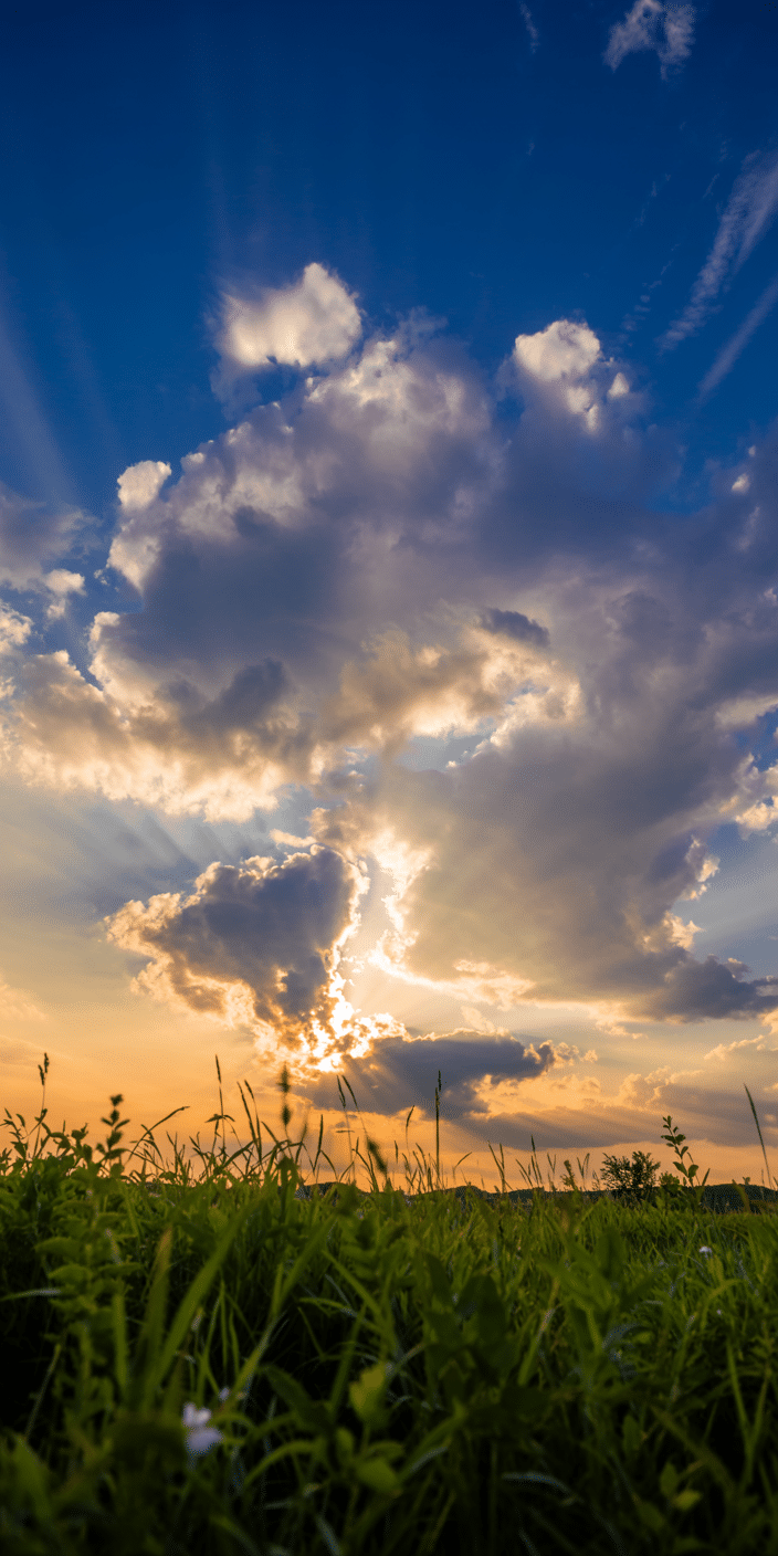 Radiating beams of sunlight break through a dramatic cloudscape above a lush green field. The contrast between the glowing sky and the grassy foreground makes this wallpaper both uplifting and grounding. It’s a beautiful option for fans of sky wallpaper 4k and background clouds.