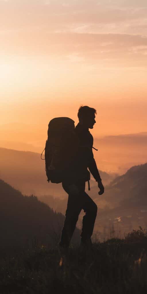 A silhouette of a solo hiker stands tall against a golden sunrise, overlooking a valley covered in morning mist and layered mountains. The soft orange and peach tones exude calm and strength, making this an ideal Phone Wallpaper For Men that inspires exploration and purpose. It’s also a powerful Military Motivation scene, symbolizing persistence, solitude, and journey. A perfect pick for iPhones with a love for nature and inner drive.