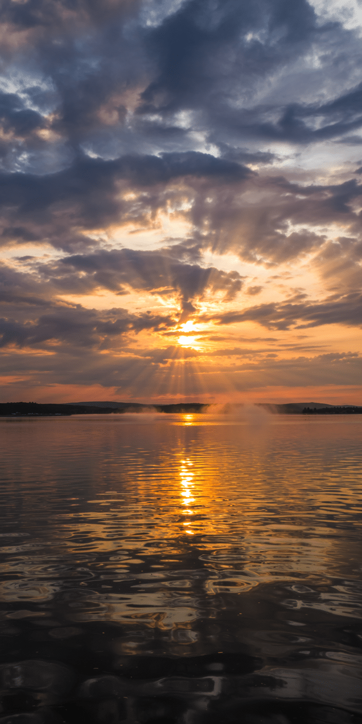 A dramatic sunset over calm waters with rays of golden light piercing through a textured sky. The scene is full of depth and emotion, making it ideal as a light lockscreen or light phone wallpaper. This natural glow pairs well with evening vibes or serene reflection, perfect for iPhone users seeking warmth and inspiration.