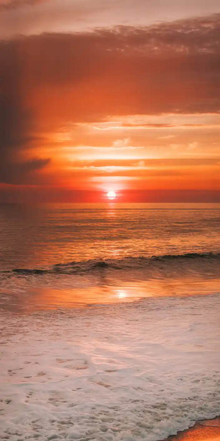 This breathtaking image captures a warm sunset dipping below the horizon, bathing the sky and ocean in glowing orange and rose hues. Ideal for lovers of the orange aesthetic, this serene scene is perfect for a calming orange phone wallpaper. Its natural gradient and peaceful waves bring a touch of golden hour magic to any iPhone or Samsung screen.